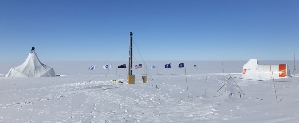 A landscape photo of Law Dome in Antarctica, surrounded by flags and flanked by tents; photo by Peter Neff.