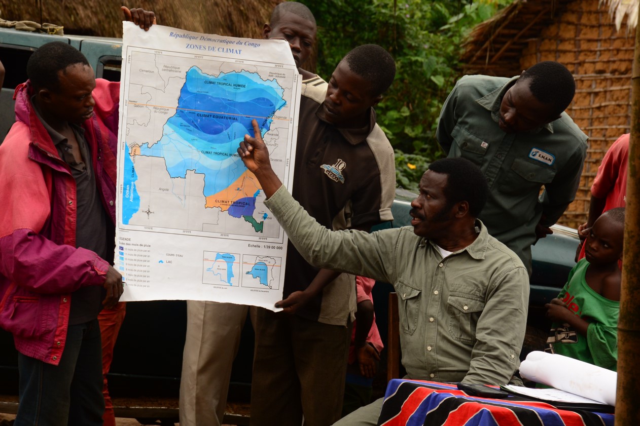 A photo of Esakakondo "Al" Lohese pointing to a climate map of the Democratic Republic of Congo