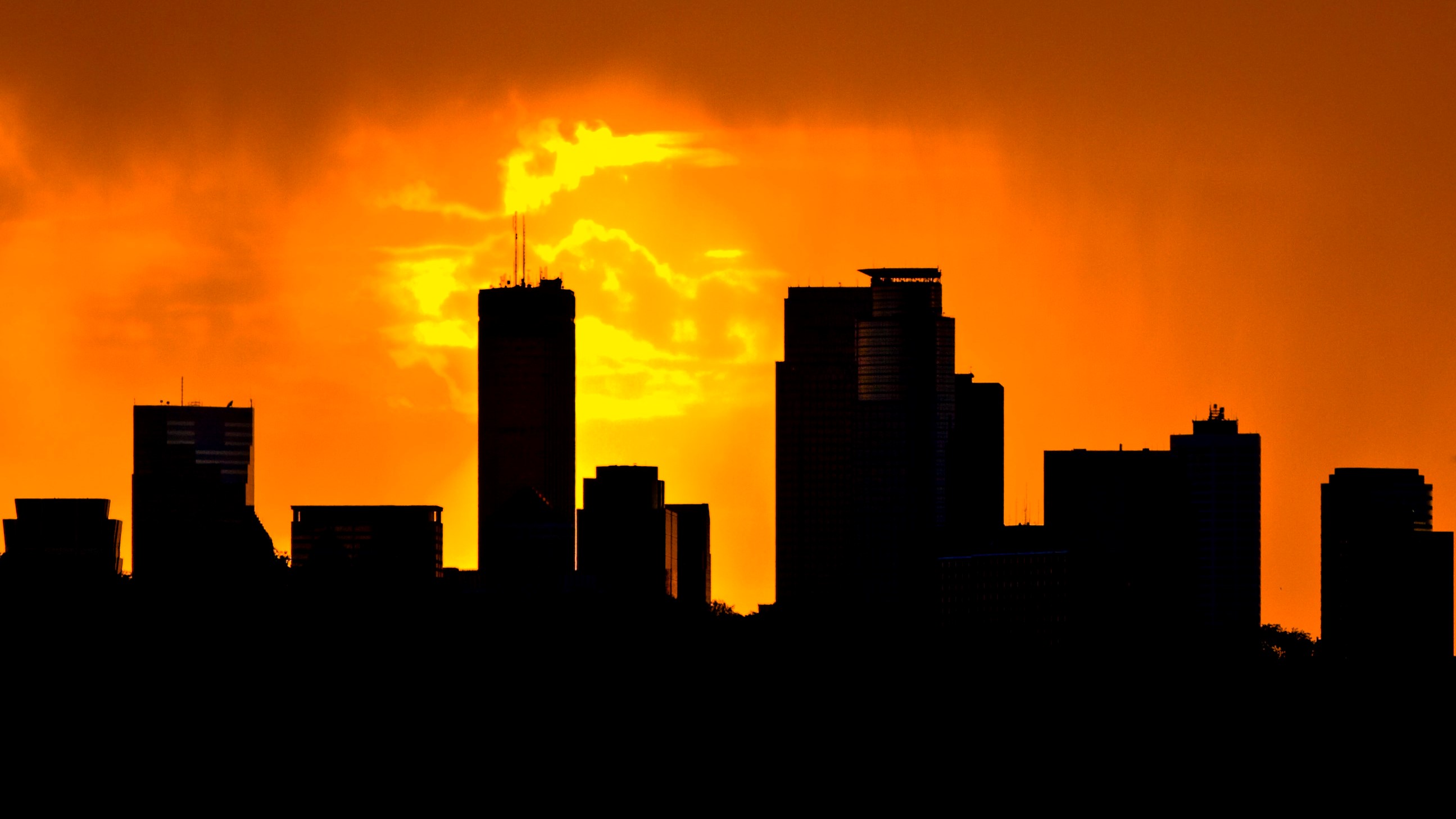 A photo of the Minneapolis skyline in silhouetted against a vibrant orange sunset; photo by Tony Webster