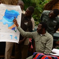 A photo of Esakakondo "Al" Lohese pointing to a climate map of the Democratic Republic of Congo