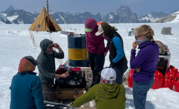 5 researchers in snow gear gather around camp at Mt. Waddington BC