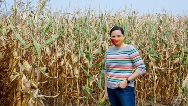 A photo of Heidi Roop standing near a corn field and wearing a mask. Credit: Audrey Rauth