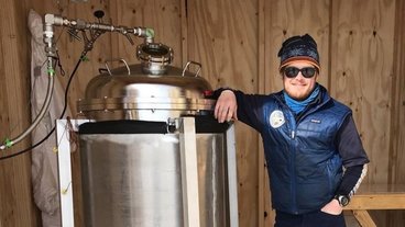 A photo of Peter Neff in cold weather gear standing next to a large vacuum chamber