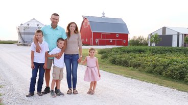 A photo of Nancy Bohl Bormann and her husband and three children in front of a red barn on their family farm in Iowa