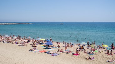 A photo of beachgoers with towels and umbrellas laying on the sand; photo by Jumilla