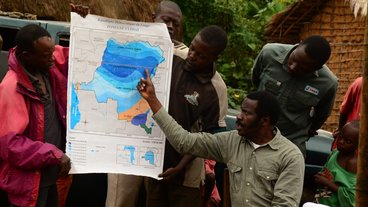 A photo of Esakakondo "Al" Lohese pointing to a climate map of the Democratic Republic of Congo.