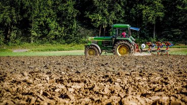 A photo of a green tractor in a field of bare soil; photo by Matthias Ripp