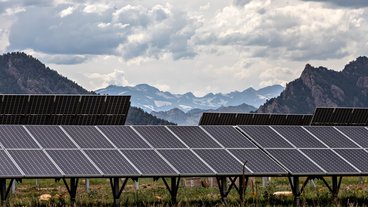 A photo of solar panels with the Rocky Mountains in the background; photo by the National Renewable Energy Lab