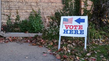 A photo of a sign that says "Vote here" with an American flag and an arrow