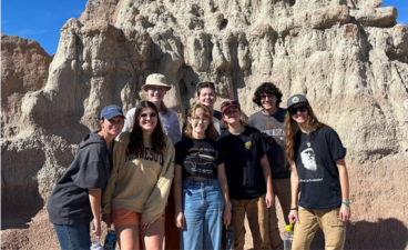 8 students are in casual clothes standing in the Badlands of South Dakota